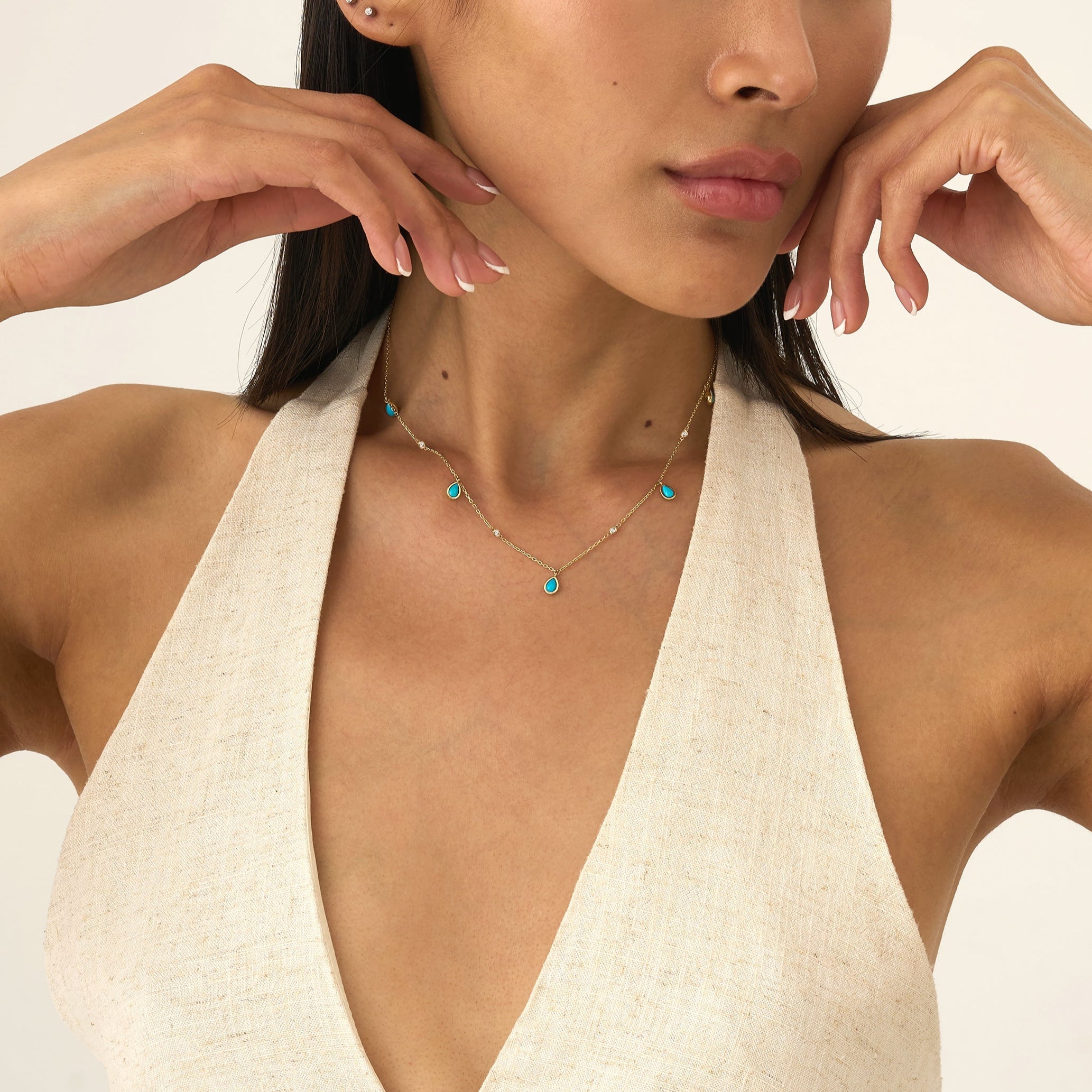 Woman wearing a necklace with turquoise stones against a neutral background