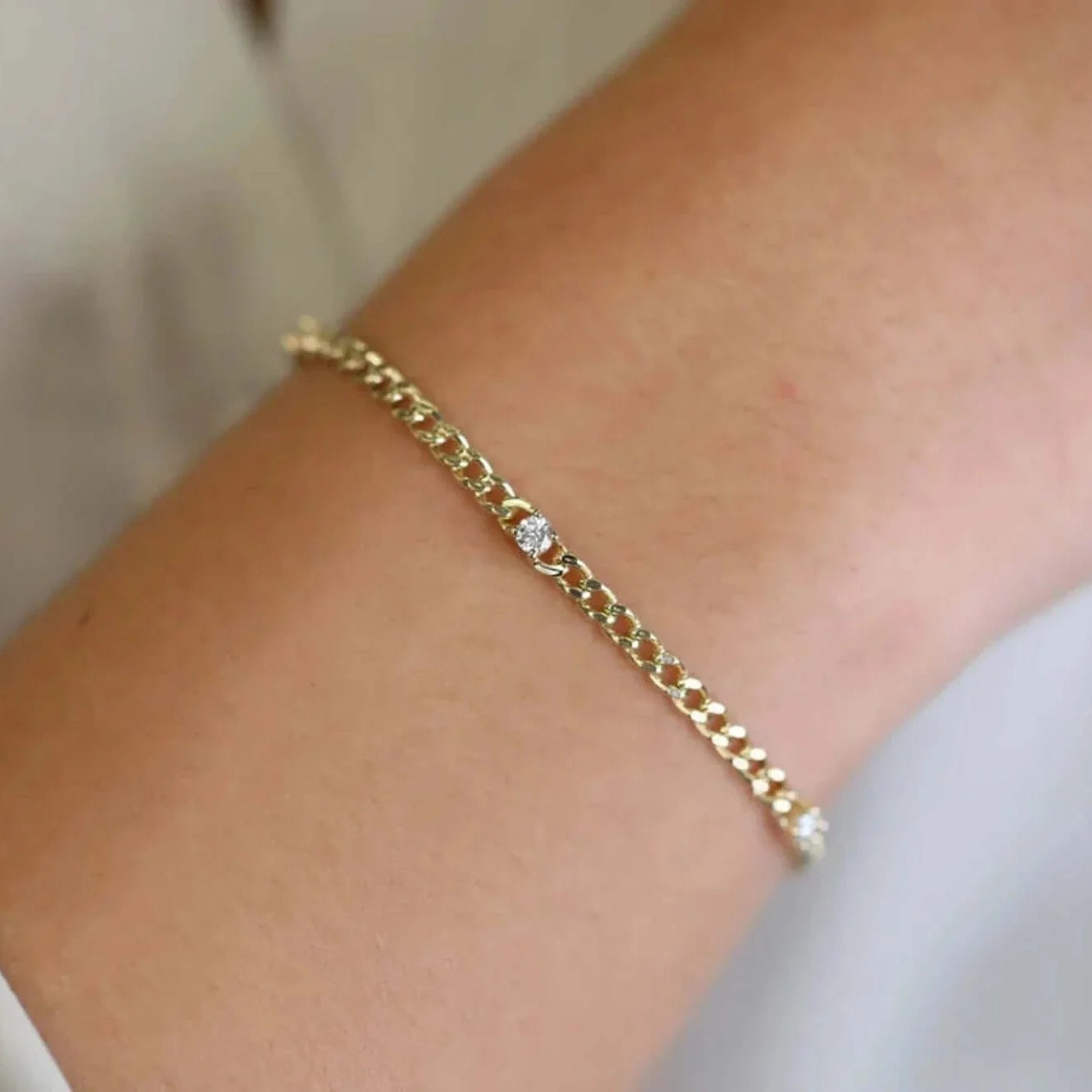 Gold bracelet with a small diamond on a wrist against a neutral background