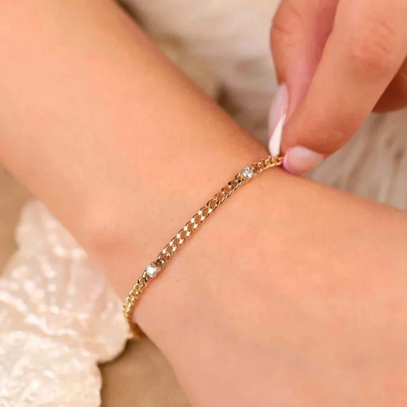 Person wearing a gold bracelet on a neutral background